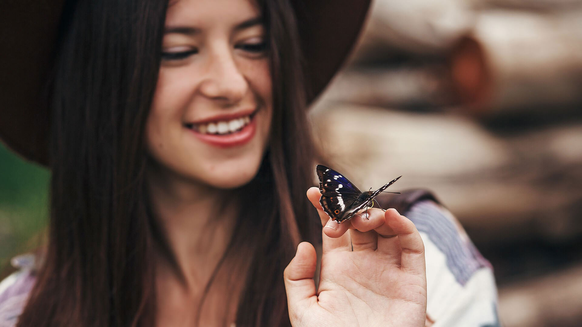 A woman holding a blue butterfly on her finger while smiling at the camera.