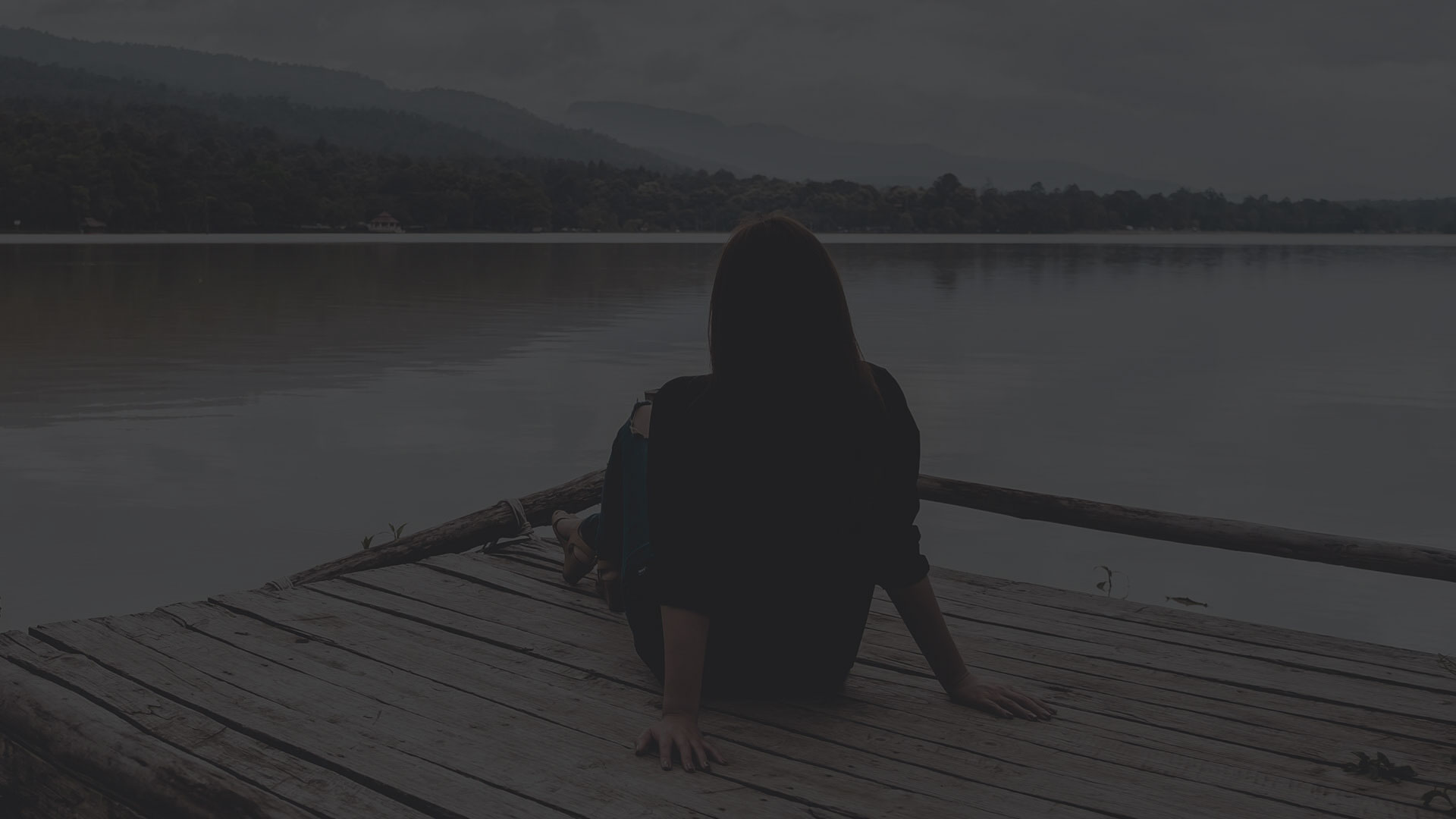 The image features a person sitting on a wooden pier with a serene lake view, set against a dark sky, with a silhouette of a figure standing behind them.